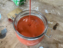 Red liquid being poured into a glass jar on a concrete surface.